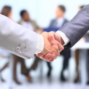 Two successful businessman shaking hands in front of corporate team at office